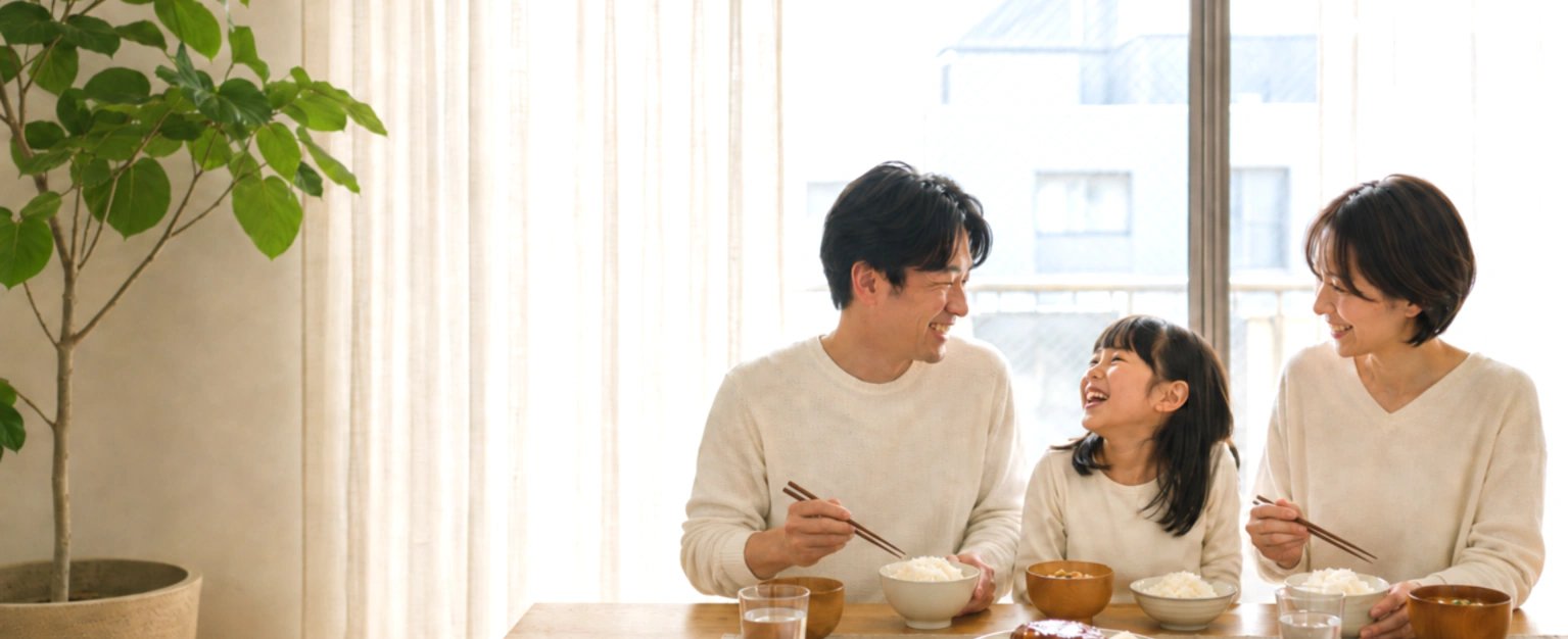 明るいダイニングで家族3人が同じおかずを囲んで食事をしている様子